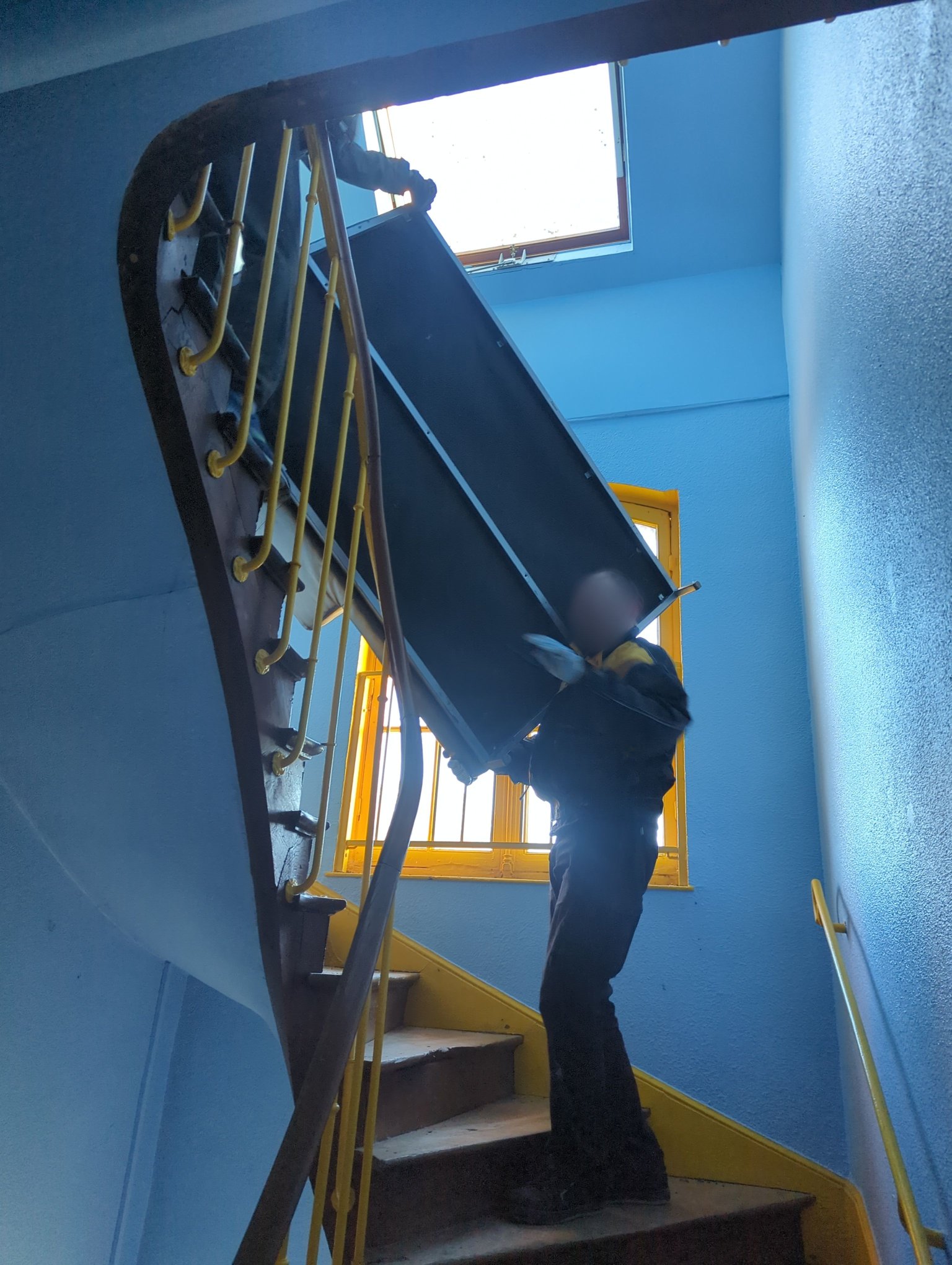 Vue en contre plongé d'un déménagement d'un canapé par deux personnes dans un escalier étroit.